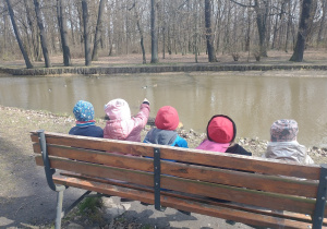 Dzieci siedzące na ławce oglądają pływające na stawie kaczki